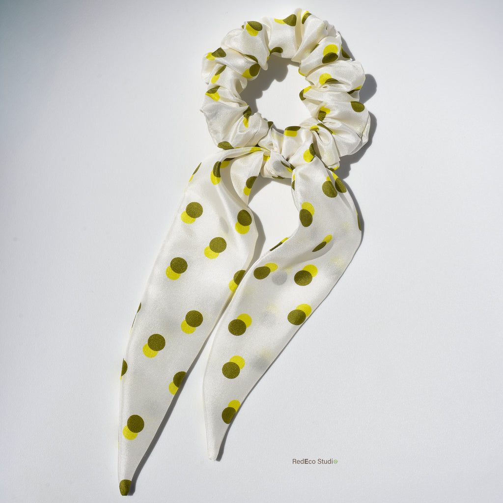 White silk hair scrunchie with green-yellow polka dots on a white background