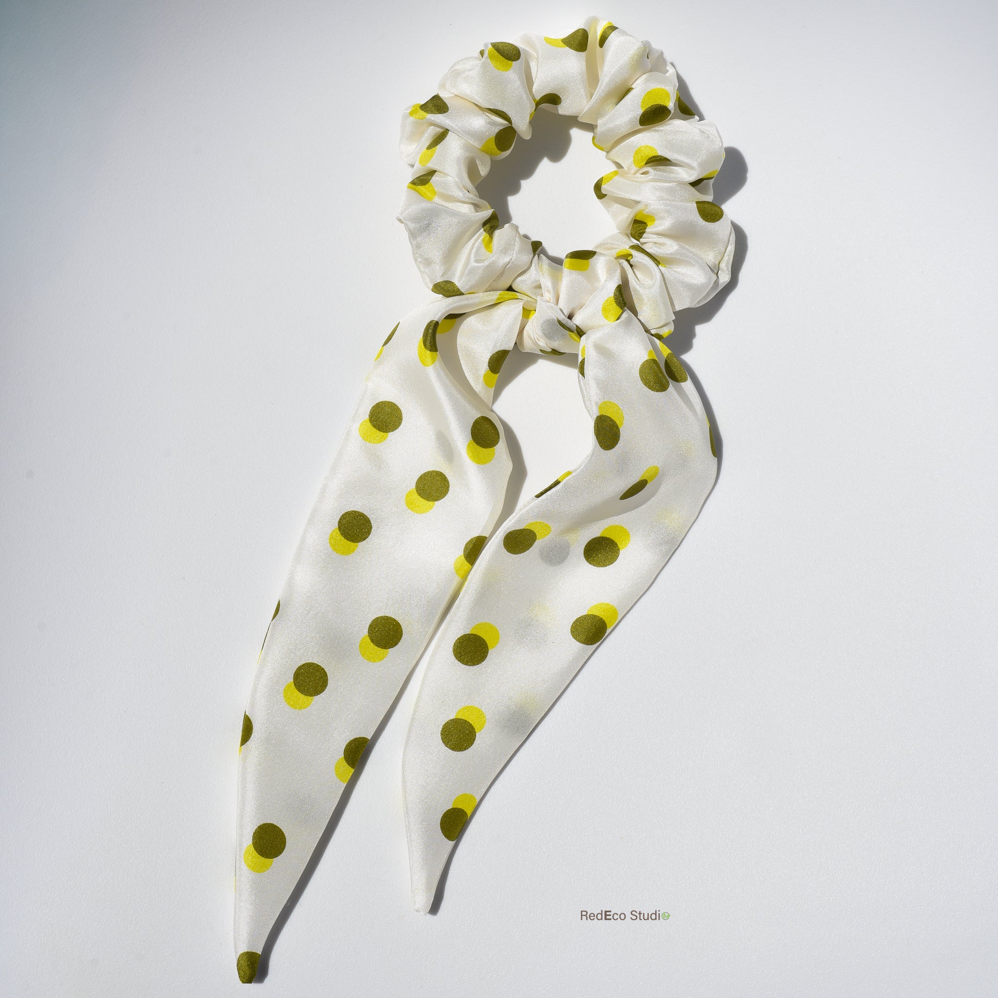 White silk hair scrunchie with green-yellow polka dots on a white background