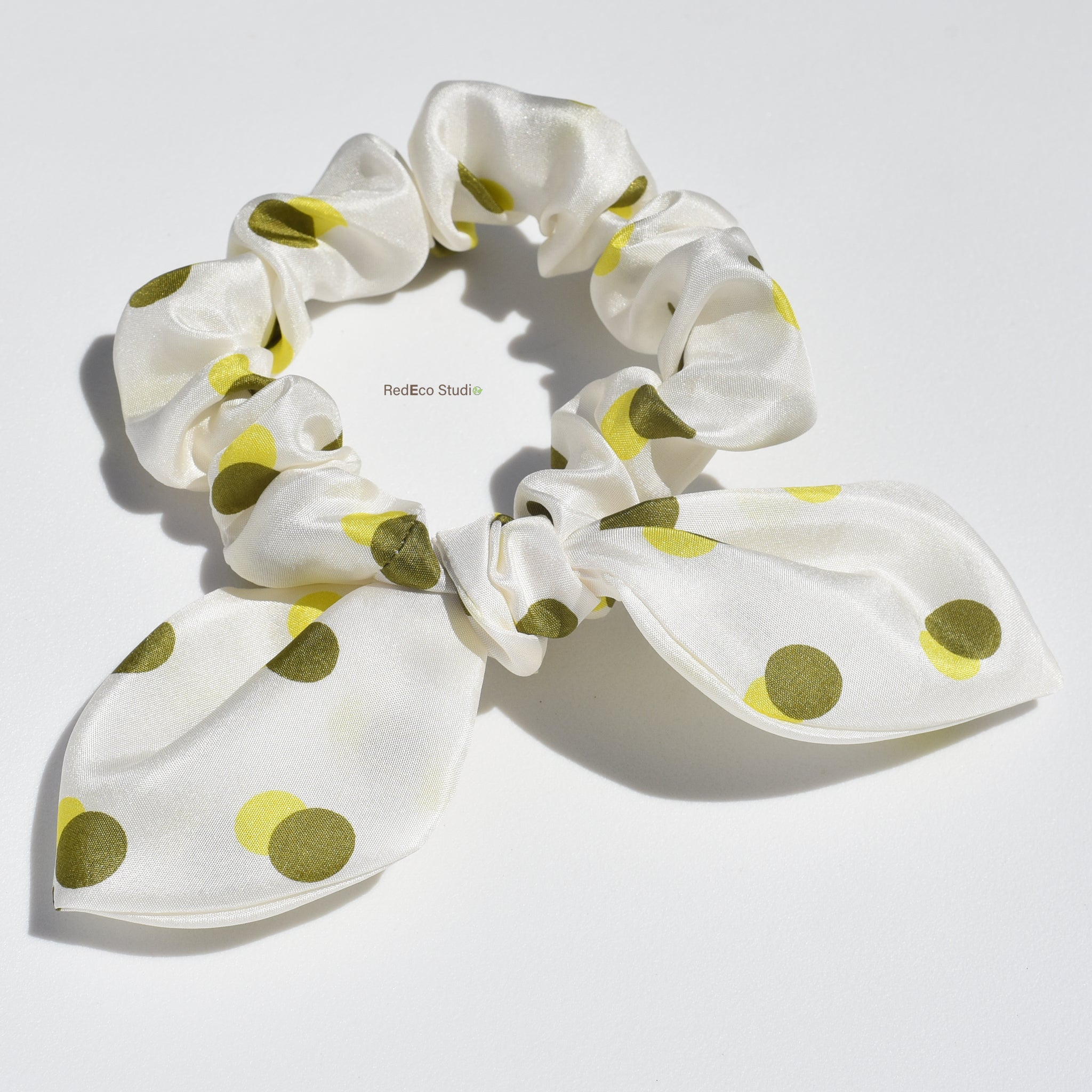 White mini silk scrunchie with green yellow polka dots on a white background