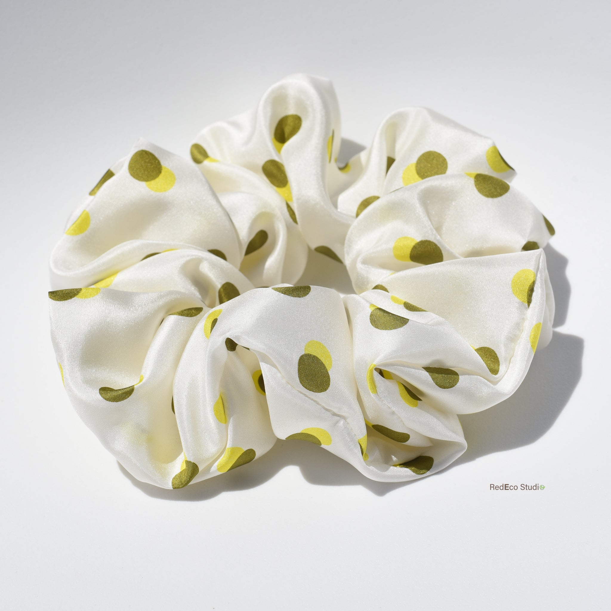 White oversized premium silk scrunchie with green polka dots on a white background