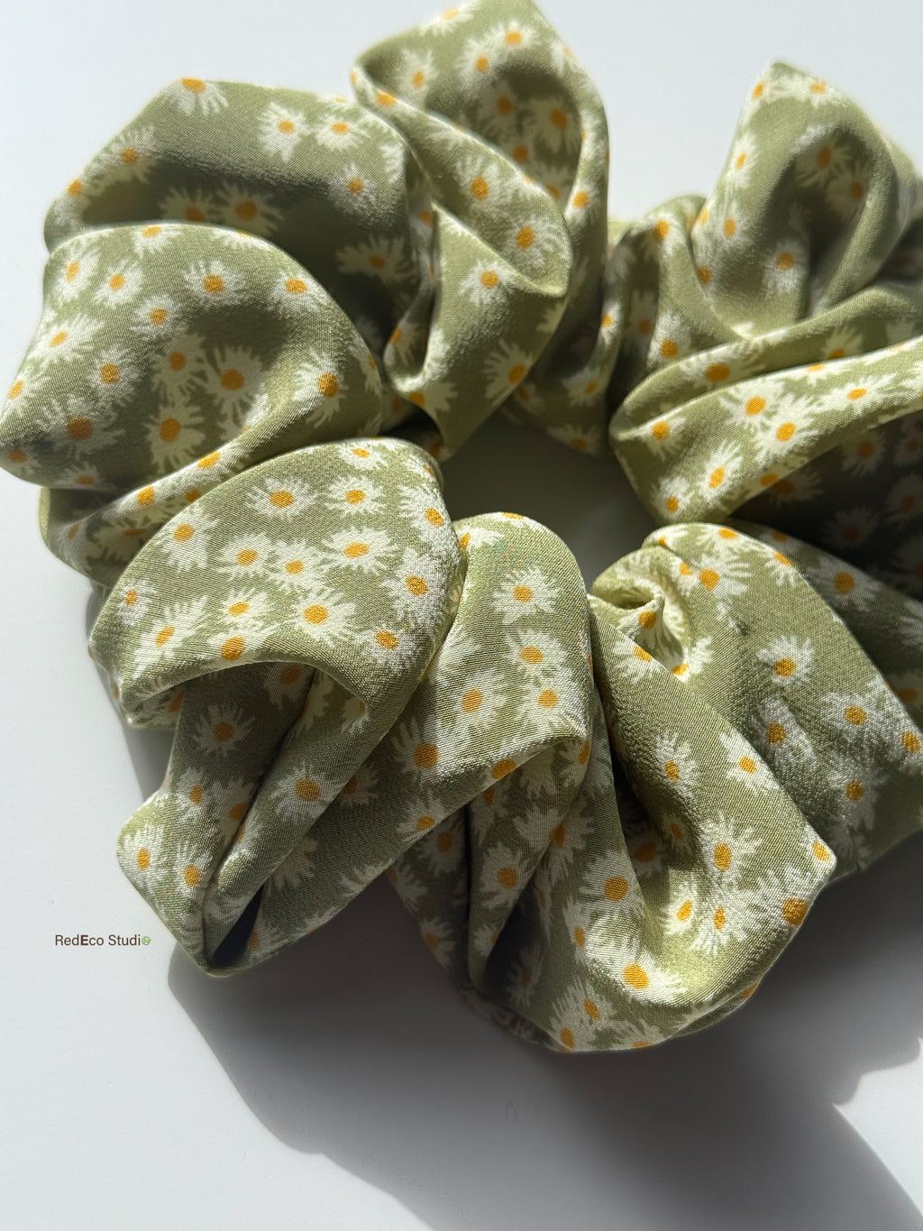 Close-up of the Matcha Daisy oversized silk scrunchie in sunlight, showing the matte crêpe de chine and daisy print