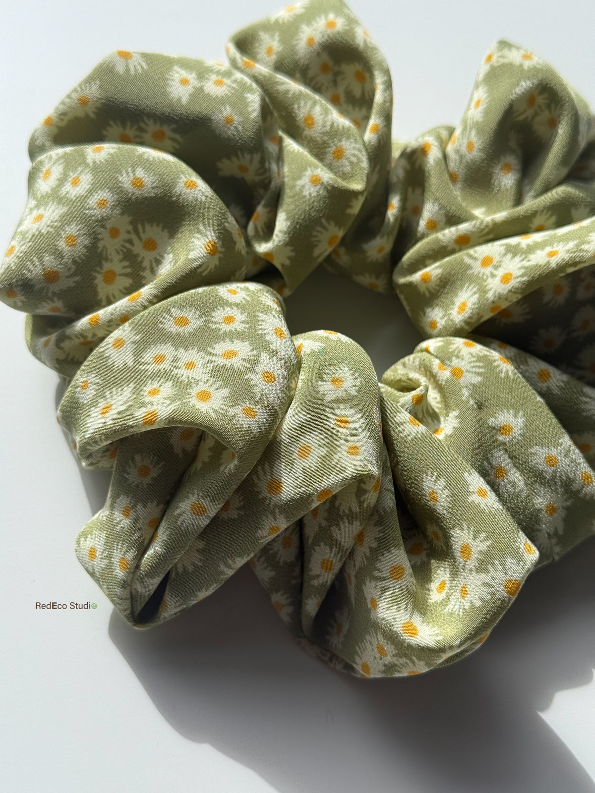 Close-up of the Matcha Daisy oversized silk scrunchie in sunlight, showing the matte crêpe de chine and daisy print