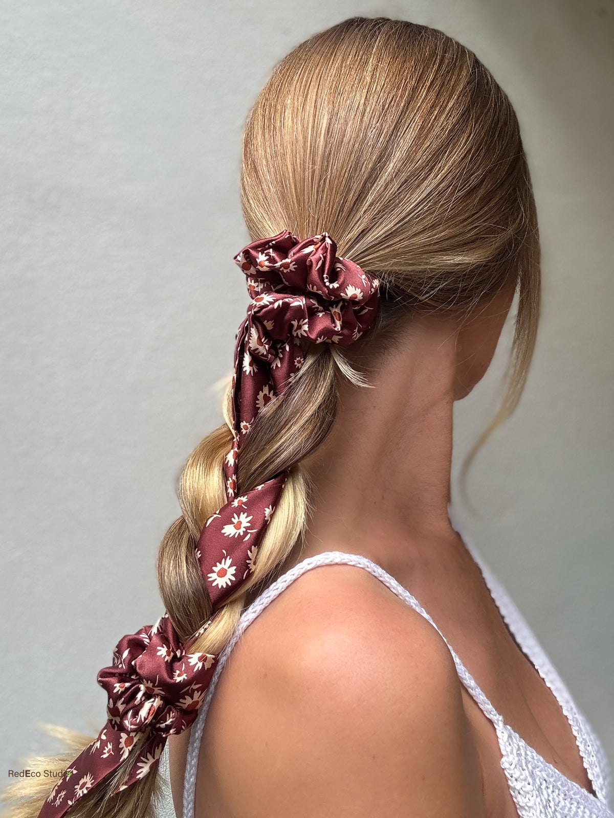 Merlot Daisy silk scarf scrunchie with its long tails woven through a loose braid, finished with a matching Merlot Daisy mini scrunchie