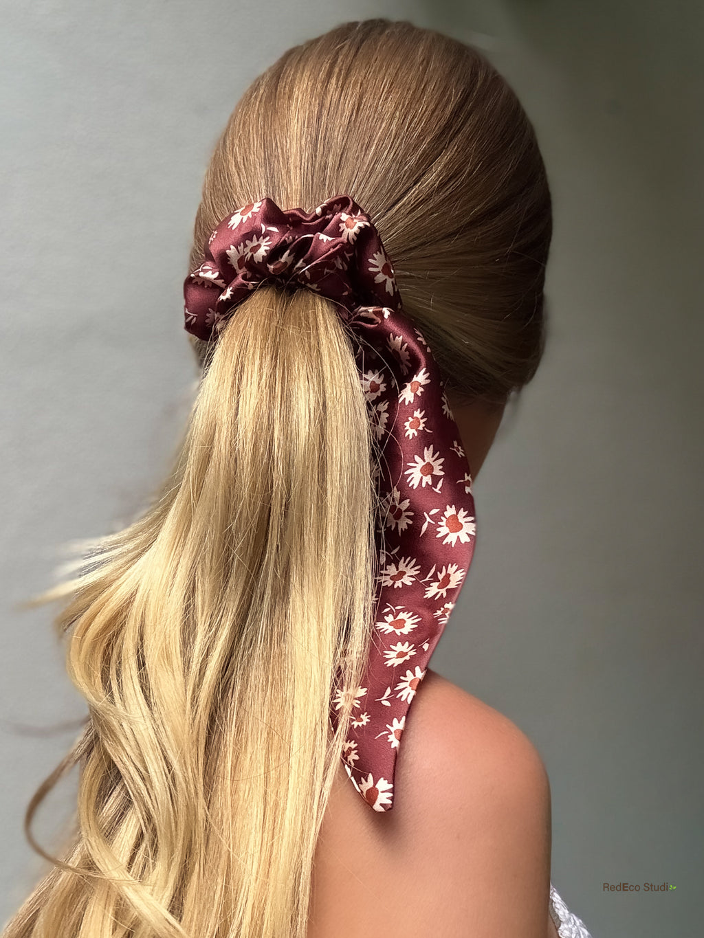 Merlot Daisy silk scarf scrunchie worn on a low ponytail, with its long burgundy daisy tails trailing over the shoulder