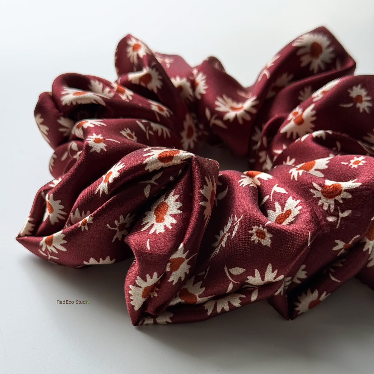 Close-up of the Merlot Daisy oversized pure silk scrunchie, angled to show the satin sheen and full gathers of the burgundy daisy print