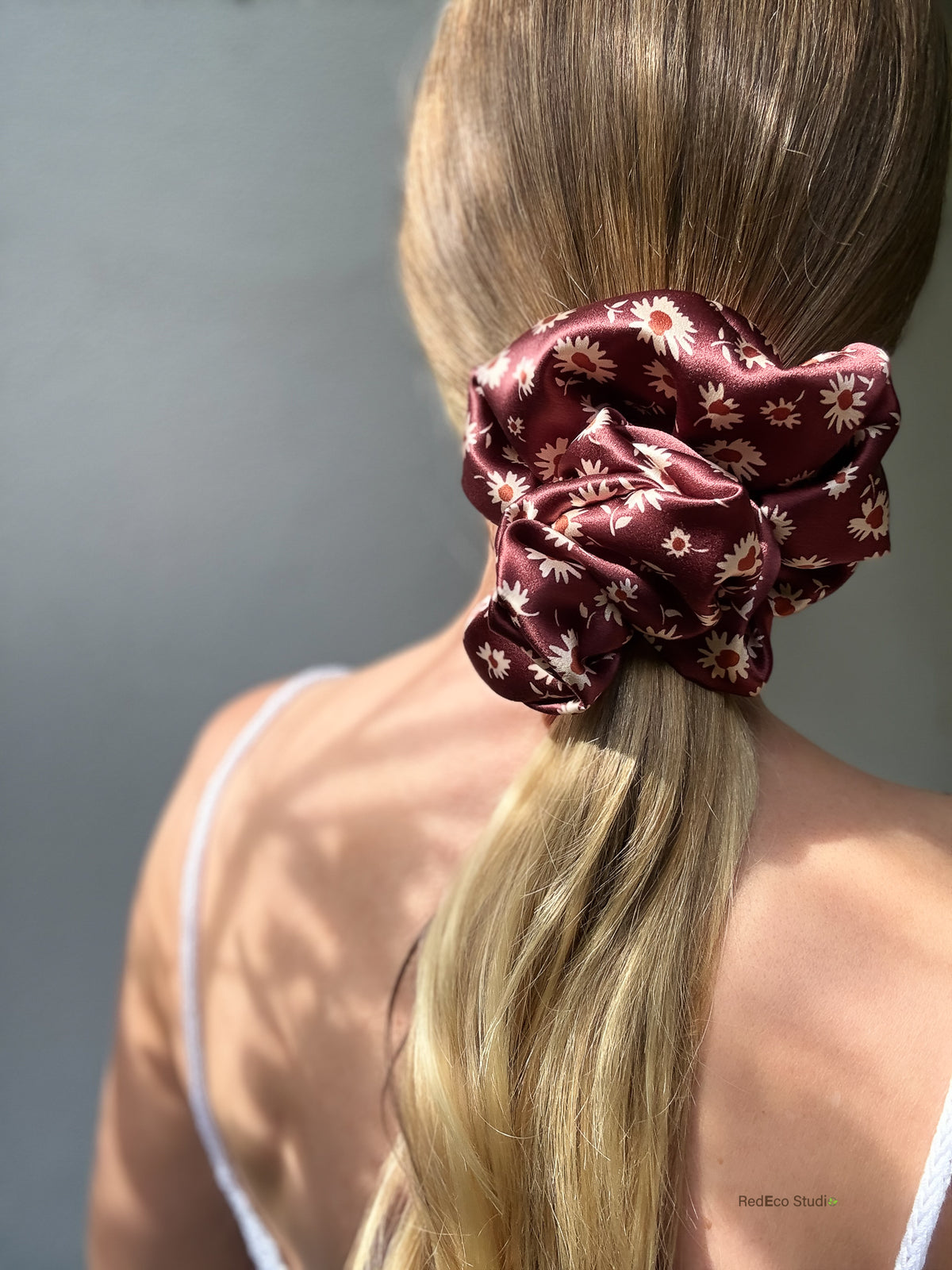 Merlot Daisy oversized silk satin scrunchie worn on a low ponytail, back view in dappled sunlight, burgundy with cream daisies