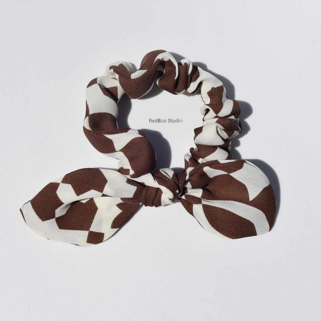 Brown and beige patterned silk scrunchie with a bow on a light gray background