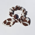 Brown and beige patterned silk scrunchie with a bow on a light gray background