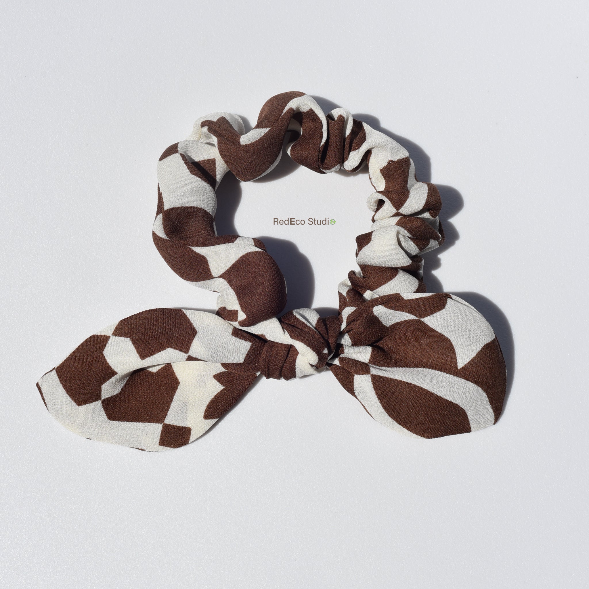 Brown and beige patterned silk scrunchie with a bow on a light gray background