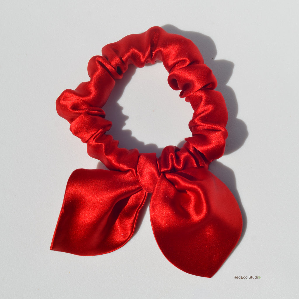 Red satin scrunchie with a bow on a light gray background