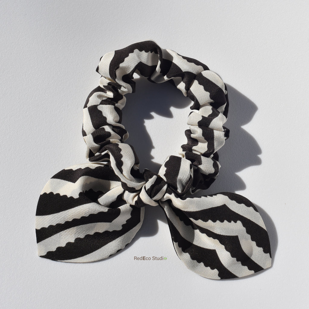 Black and white striped silk scrunchie with a bow on a light gray background
