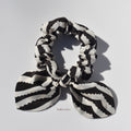 Black and white striped silk scrunchie with a bow on a light gray background
