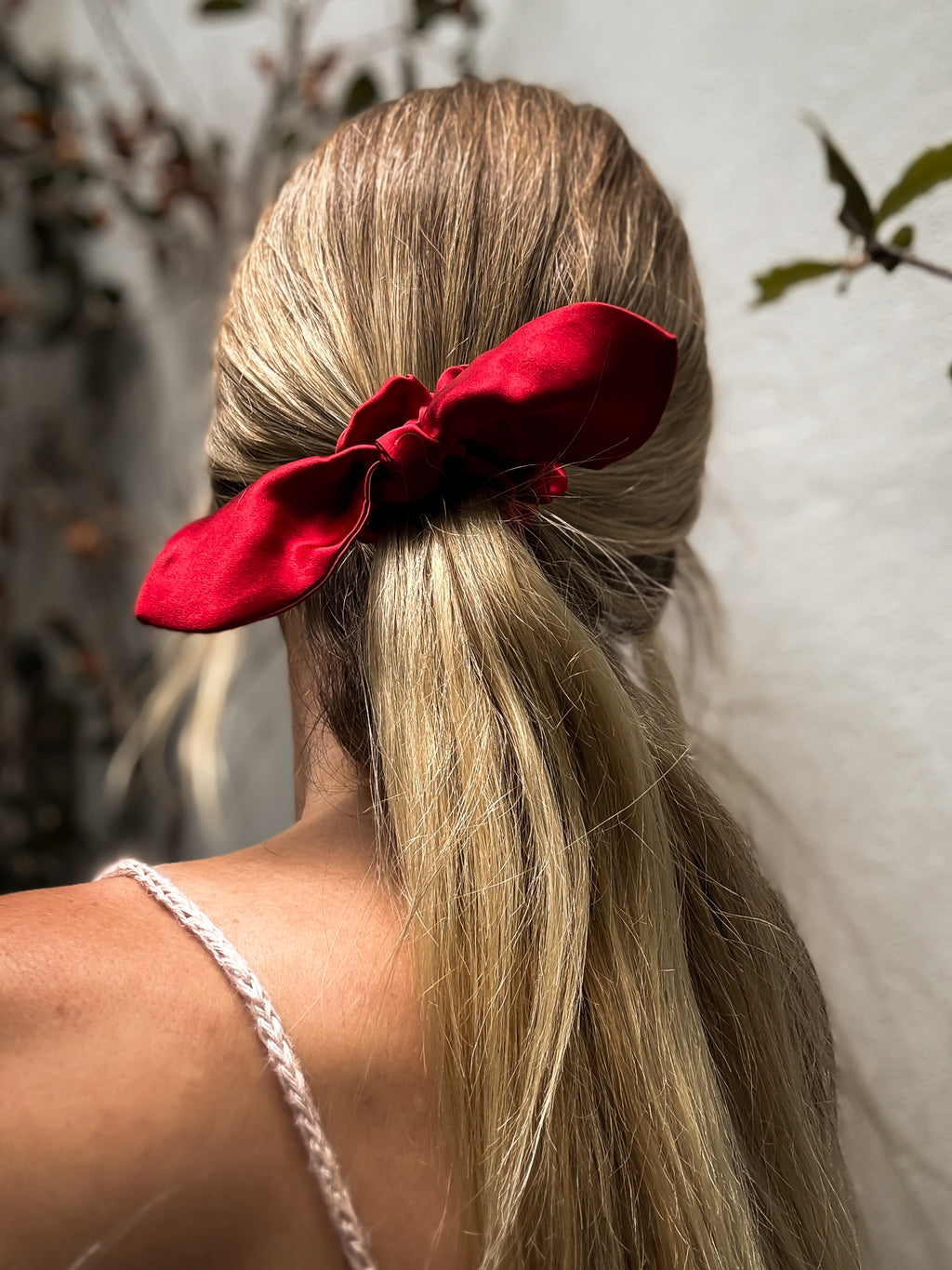 Person with blonde hair tied back with a red scrunchie against a neutral background