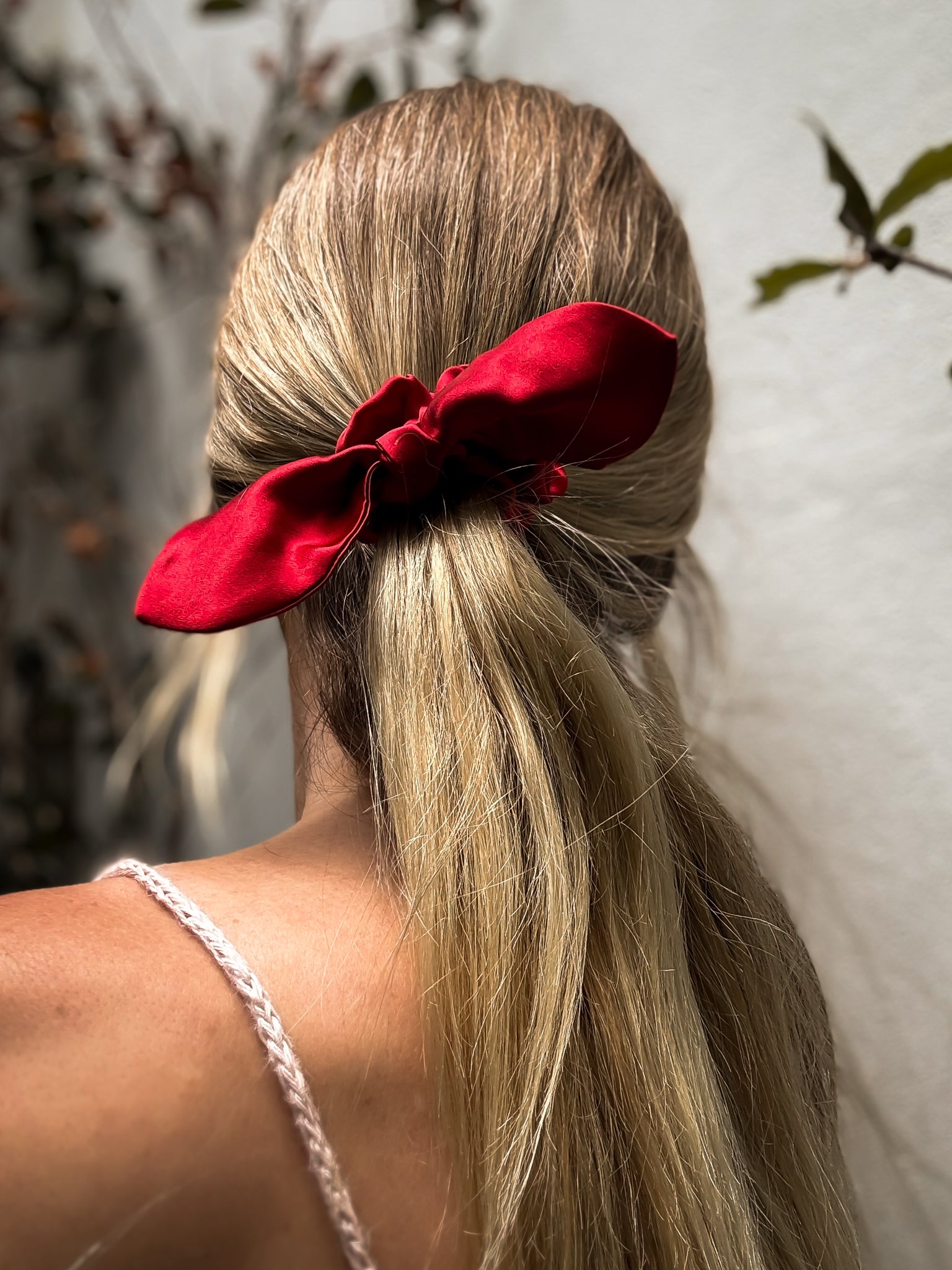 Person with blonde hair tied back with a red scrunchie against a neutral background