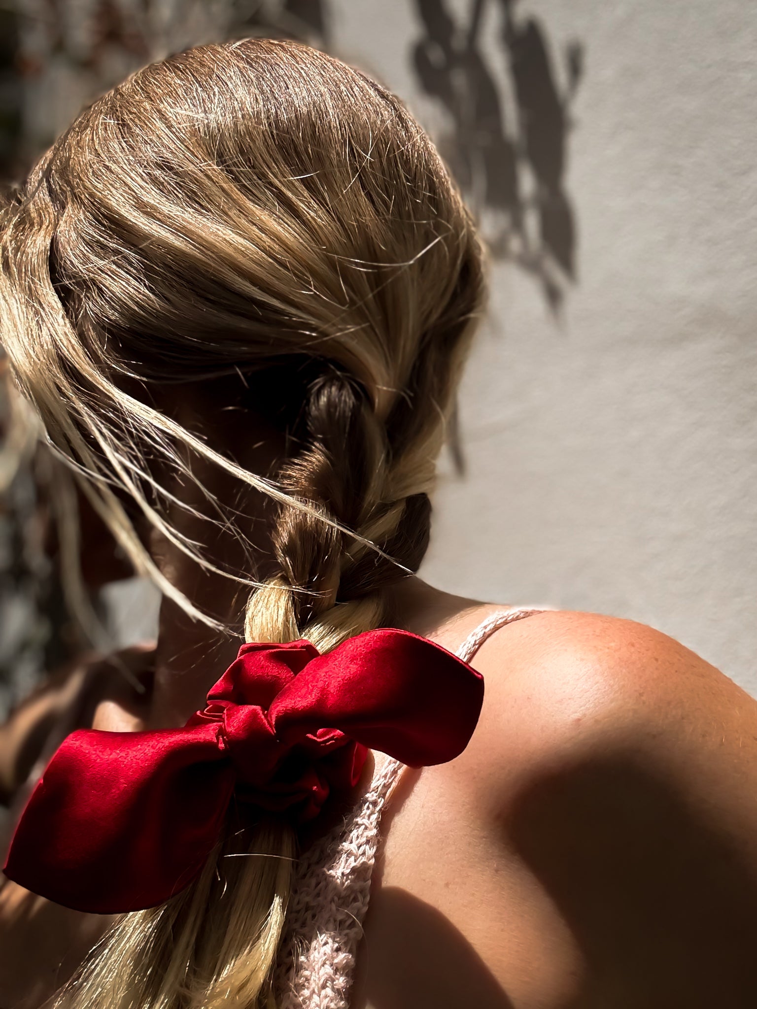 Person with braided hair tied with a red scrunchie against a neutral background