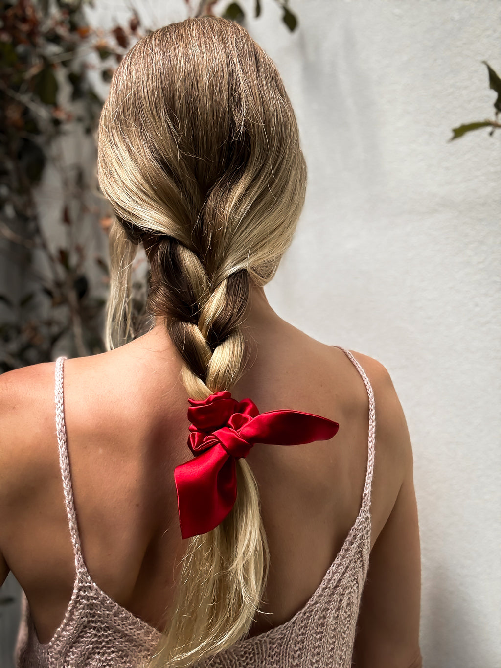 Person with braided hair and red ribbon, wearing a beige top, against a light background.