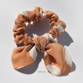 Brown and beige patterned silk scrunchie with bow on a light gray background