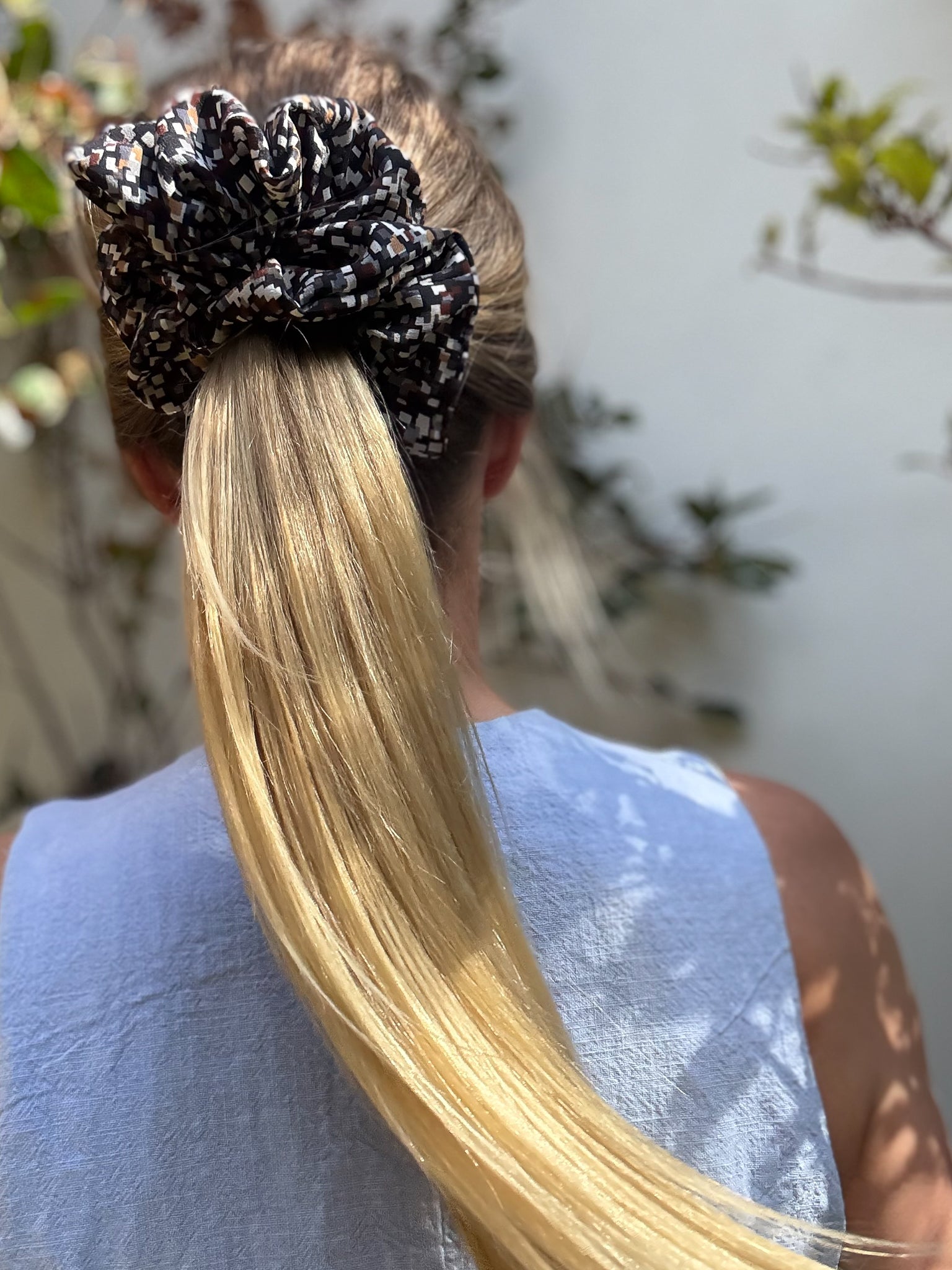 Person with a high ponytail wearing a large patterned scrunchie, blurred outdoor background