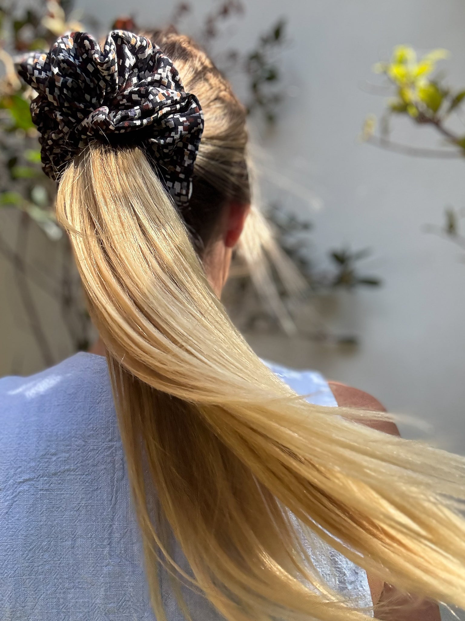 Person with blonde hair tied up with a silk hair silk scrunchie against a blurred natural background