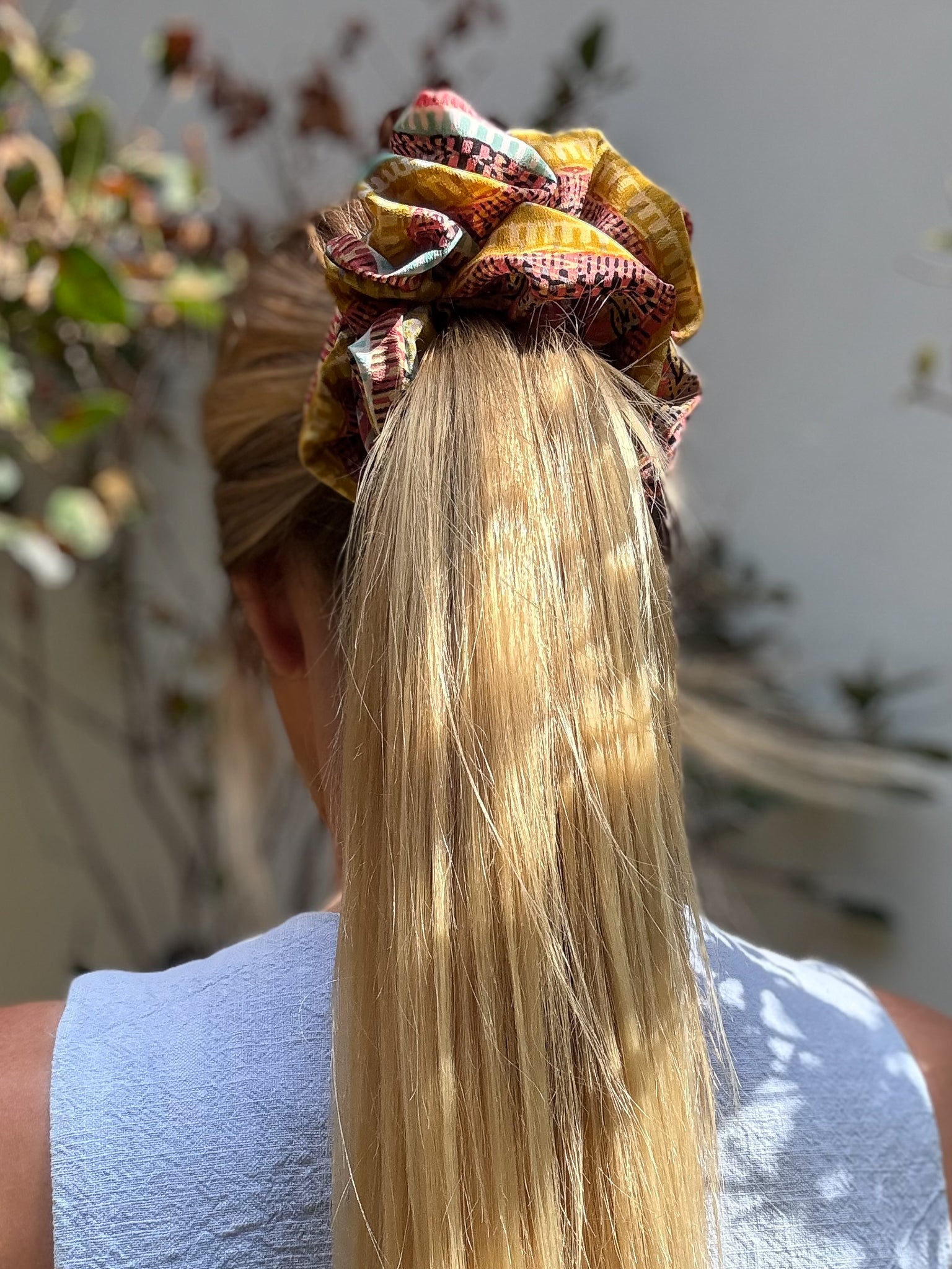 Person with a colorful large silk scrunchie in their hair, standing outdoors.