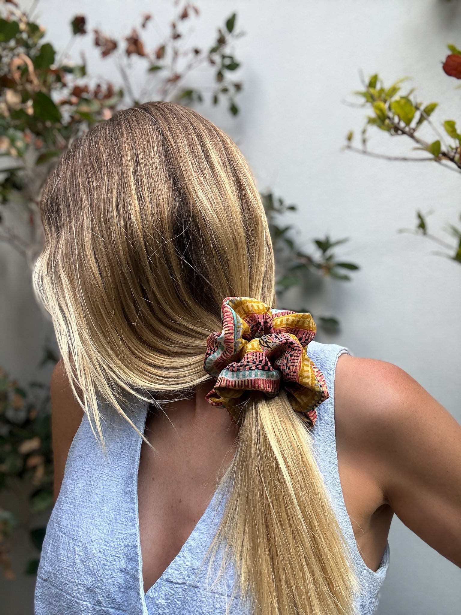 Person with blonde hair tied in a ponytail with a colorful xl silk scrunchie, outdoors.