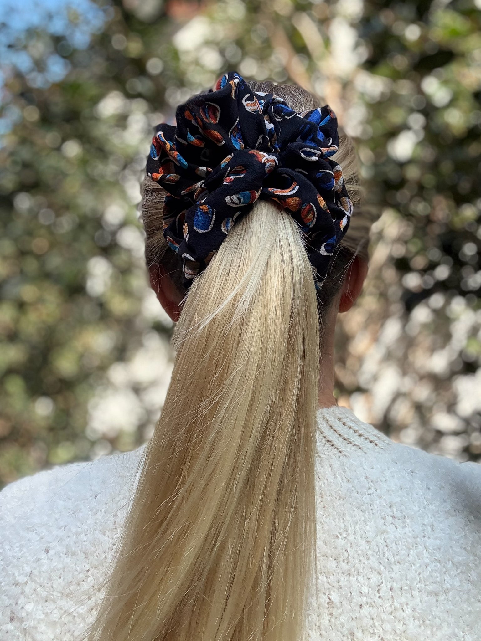 Person with a high ponytail wearing a patterned silk scrunchie, blurred natural background