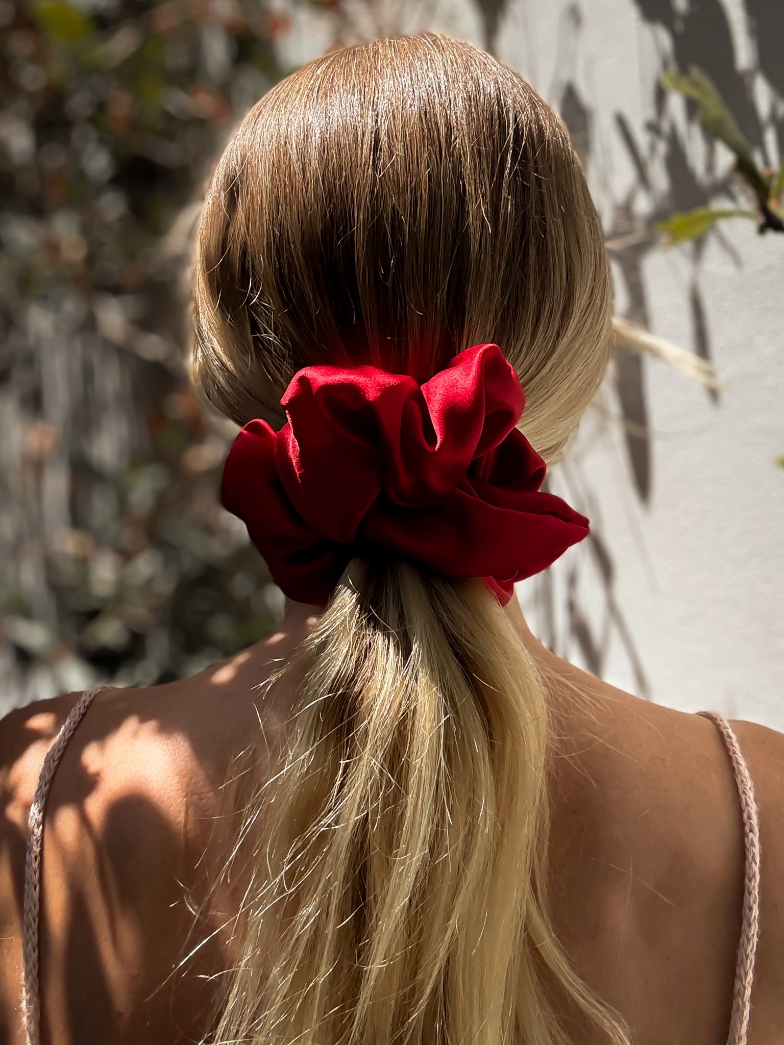 Person with a red scrunchie in their blonde hair against a natural background