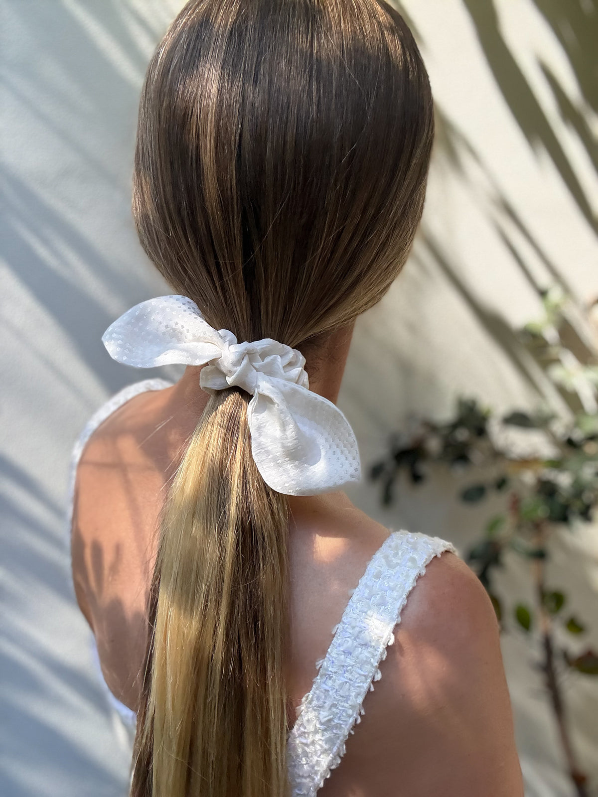 Pearl Reverie mini silk bow scrunchie tied on a low ponytail in soft sunlight, back view