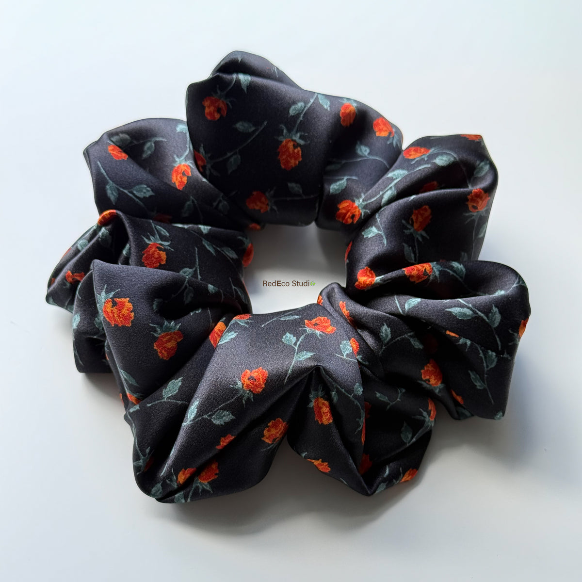 Rosebud Noir oversized pure silk scrunchie, black satin with small red roses and green stems, angled view