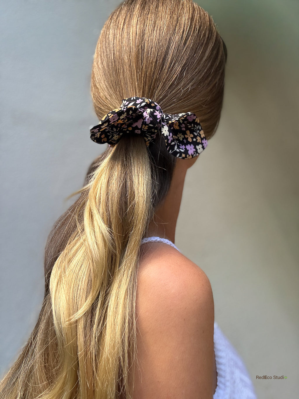 Side profile of a long low ponytail tied with the Violet Meadow mini silk georgette bow scrunchie, lilac and apricot flowers on black