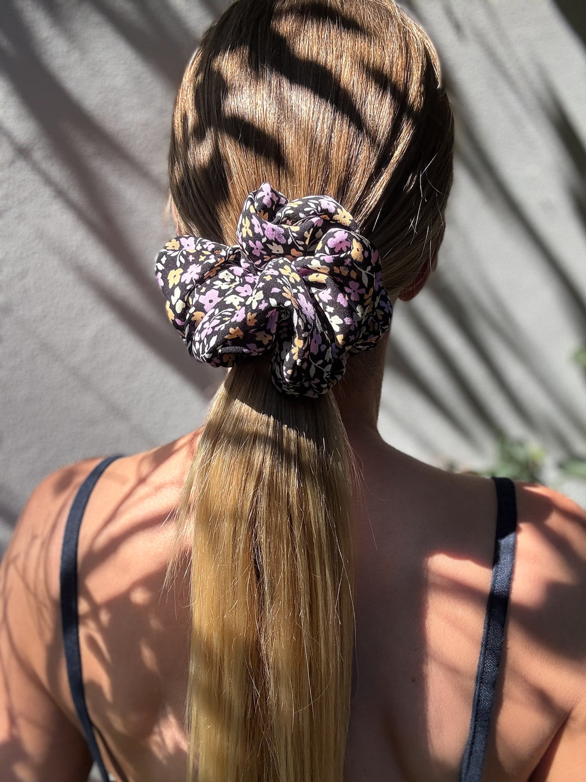 Violet Meadow oversized silk scrunchie on a low ponytail, back view with leaf shadows in the sun